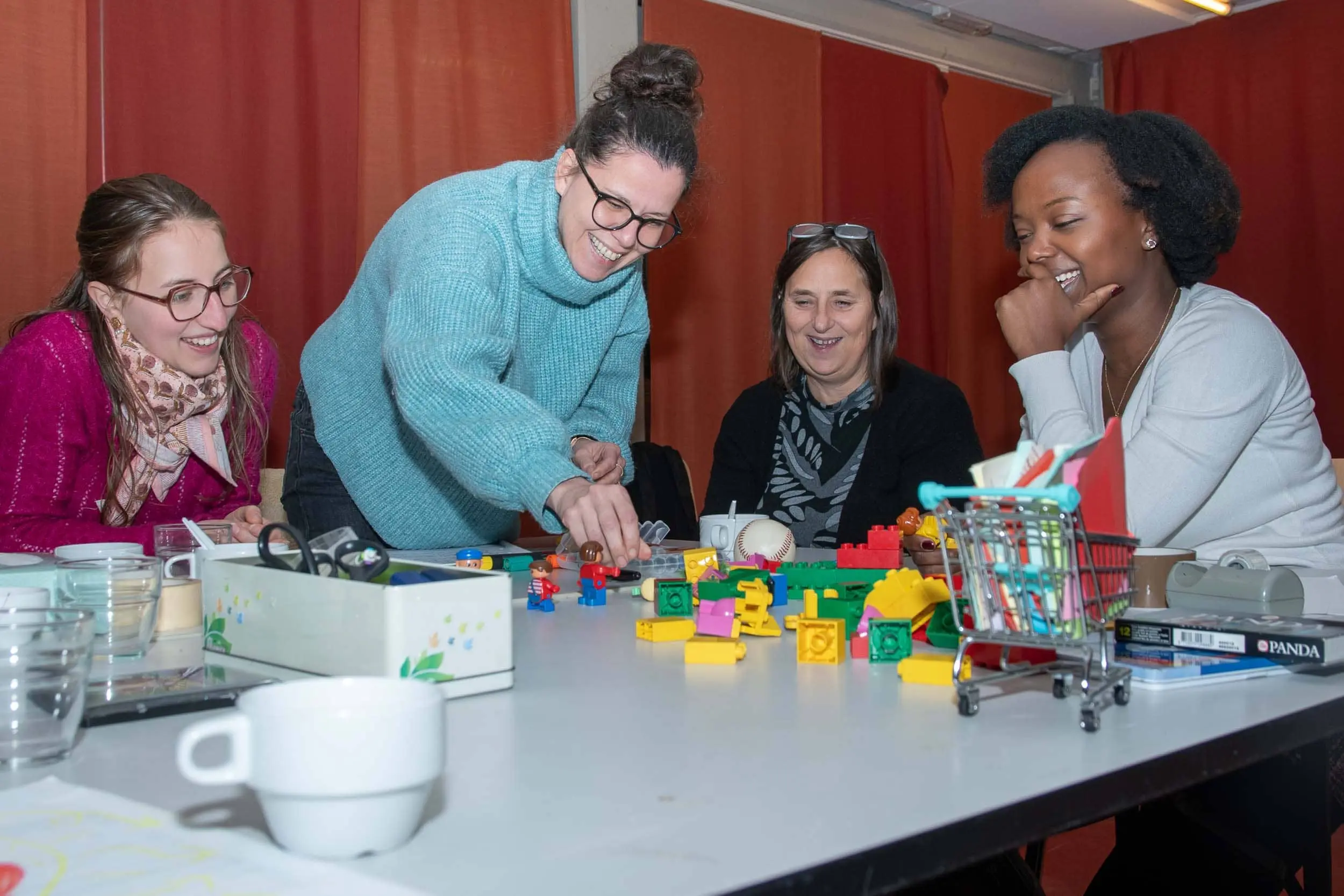 Une photo de 4 participantes à l’atelier de découverte des outils d’intelligence collective rient ensemble d’une situation représentée avec des lego. oplic asbl à Bruxelles Belgique